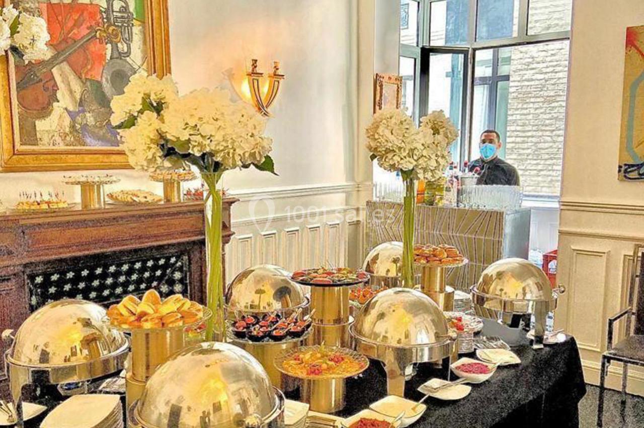 Buffet élégant avec plats variés sous cloches, décoré de fleurs blanches dans une salle lumineuse.