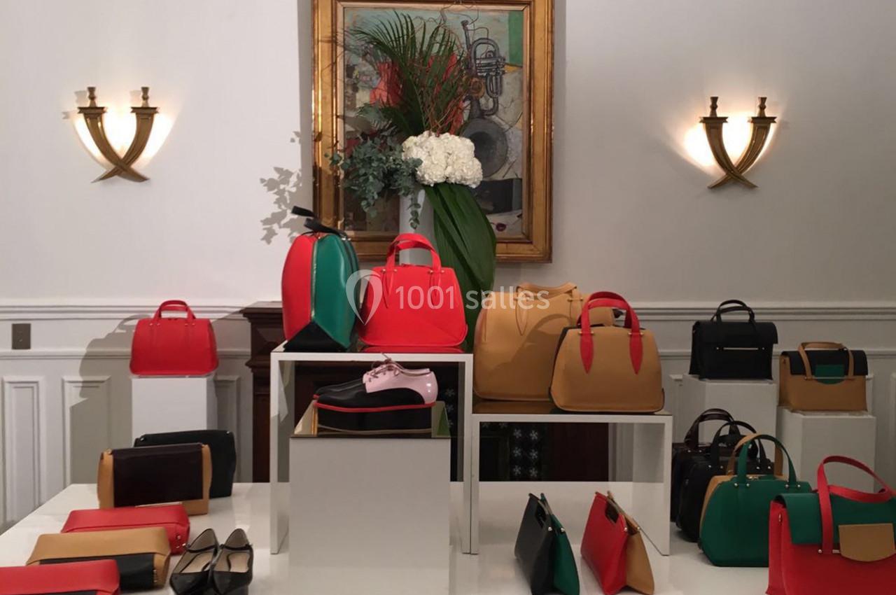 Collection de sacs à main colorés et accessoires exposés sur des présentoirs dans une pièce élégante.