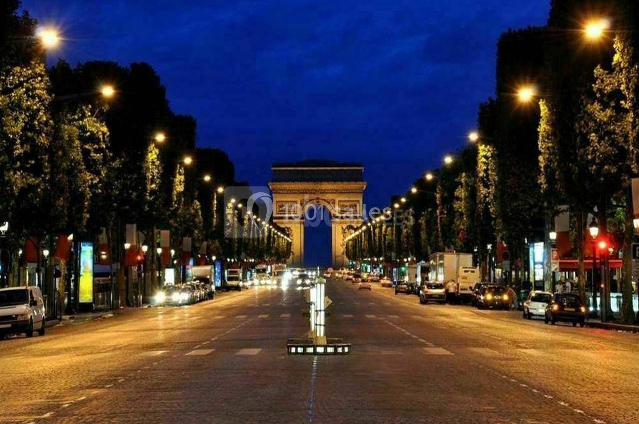 Vue nocturne de l'Avenue des Champs-Élysées illuminée, avec l'Arc de Triomphe en arrière-plan.
