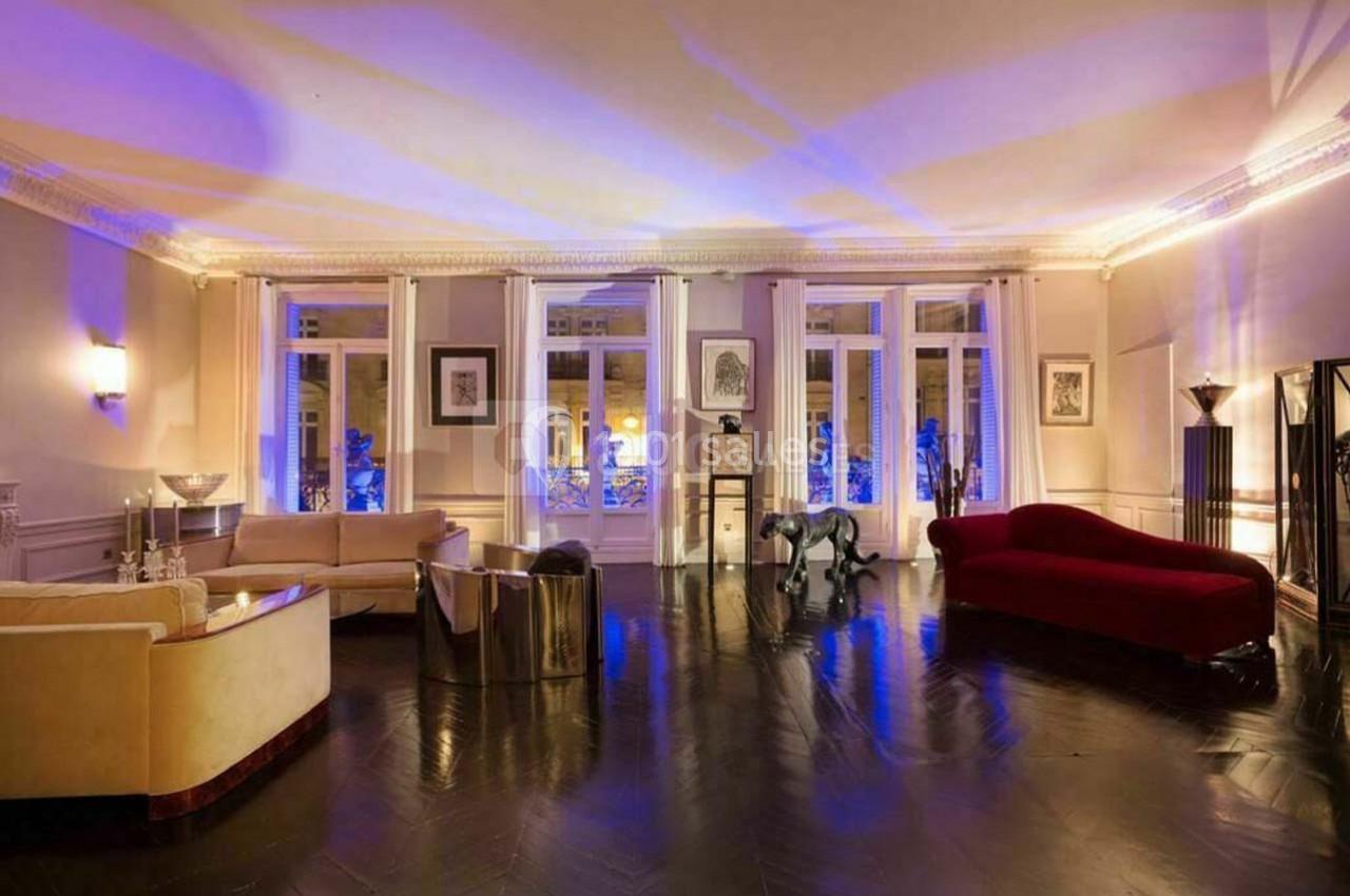 Salon spacieux avec parquet sombre, canapés clairs, canapé rouge, éclairage tamisé et grandes fenêtres.