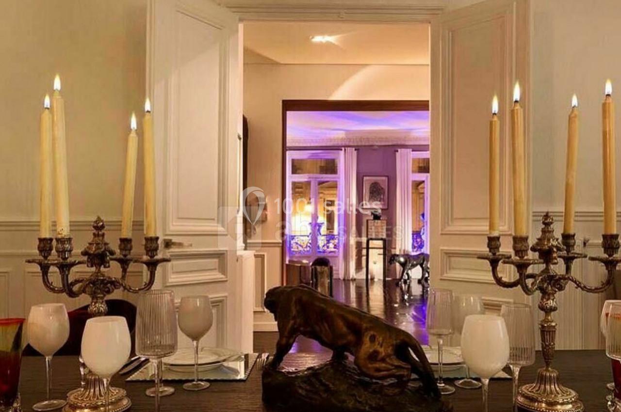 Table dressée avec chandeliers, verres et statue de taureau, dans une pièce élégante ouverte sur un salon éclairé.