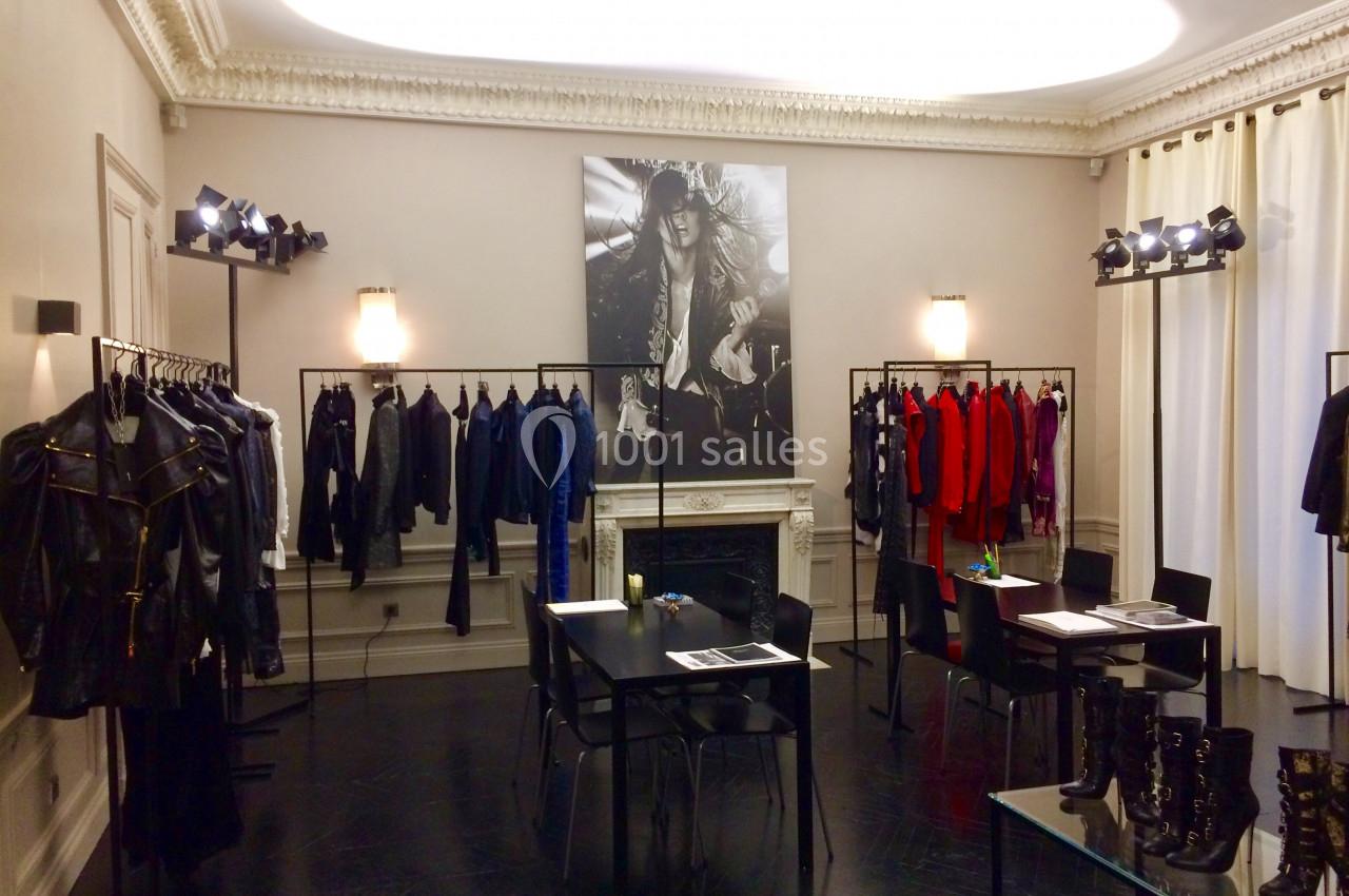 Salle d'exposition avec vêtements sur portants, tables noires et photo en noir et blanc accrochée au mur.