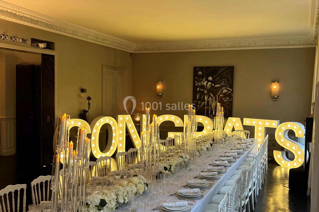 Grande table de réception élégamment dressée avec des fleurs blanches et des lettres lumineuses formant ’CONGRATS’ en…