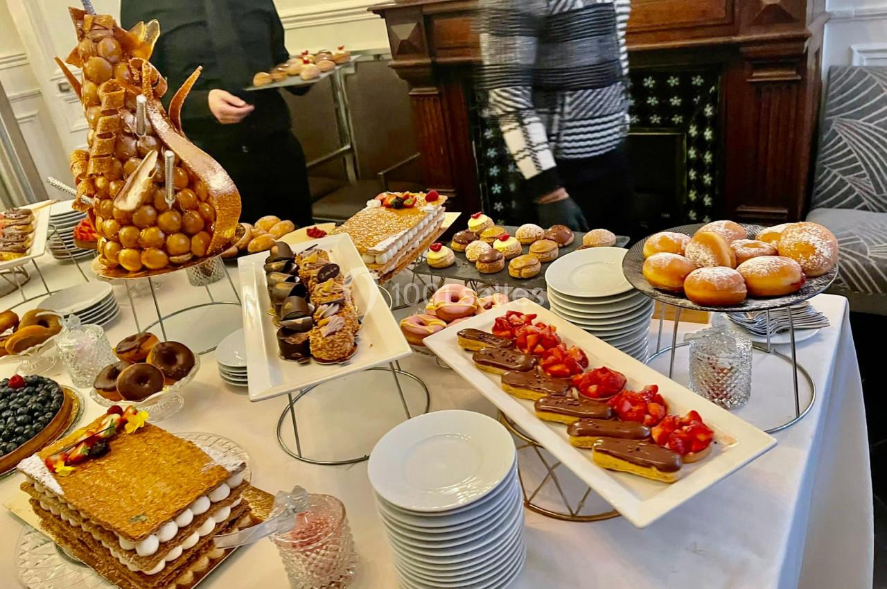 Table garnie de pâtisseries variées, dont éclairs, mille-feuilles, choux et beignets, dans un cadre élégant.