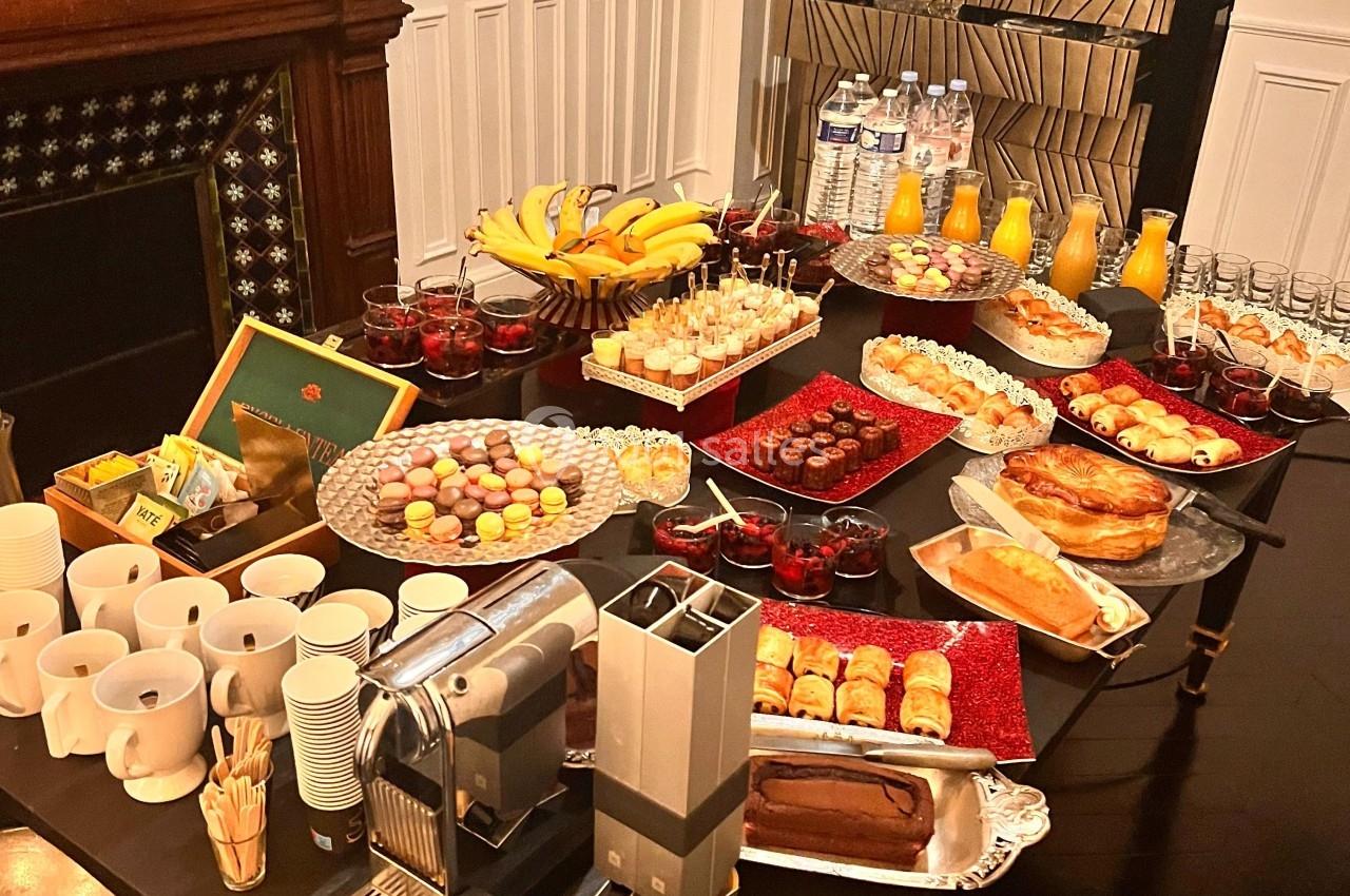 Table garnie d'un buffet varié comprenant viennoiseries, fruits, desserts, boissons et machine à café dans une salle…