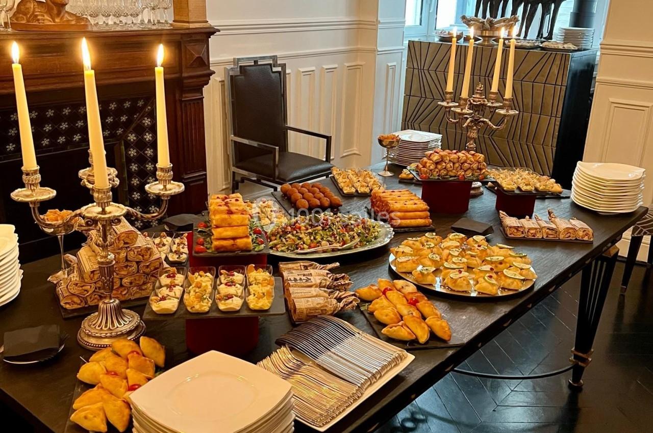 Table garnie de divers plats sucrés et salés, entourée de chandeliers allumés dans une salle élégante.
