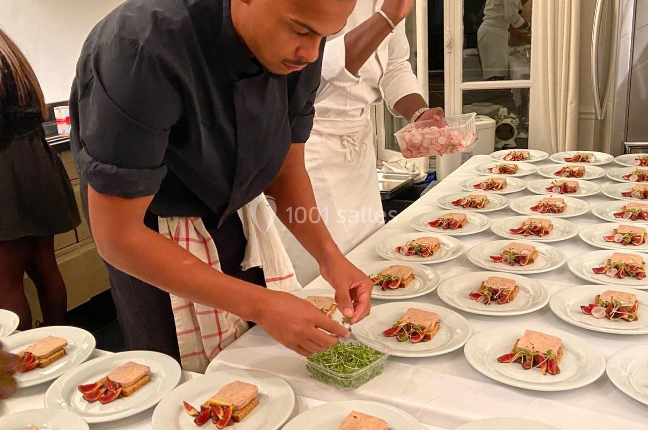 Deux chefs préparent des assiettes garnies de foie gras, figues et pousses vertes dans une cuisine professionnelle.