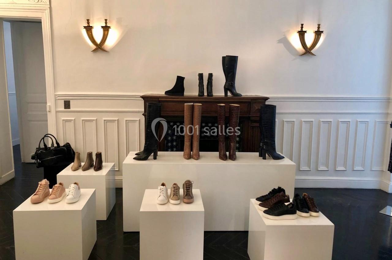 Exposition de chaussures et bottes variées disposées sur des socles blancs dans une pièce élégante avec murs blancs.