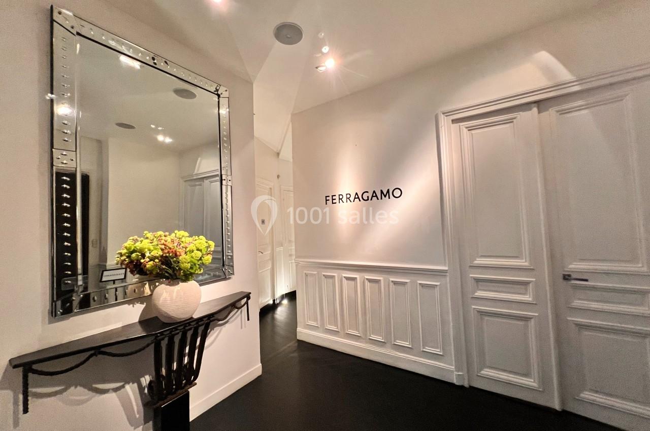 Entrée élégante avec un miroir encadré, une console décorée de fleurs et le logo Ferragamo sur un mur blanc.