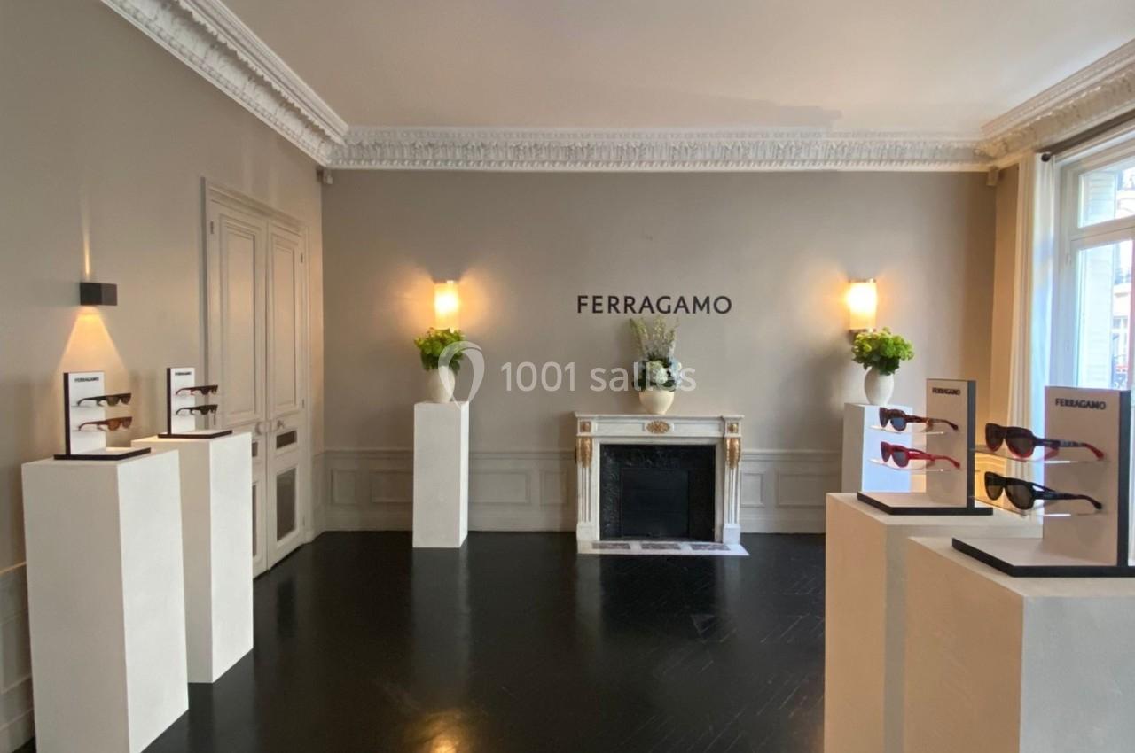 Salle d'exposition lumineuse avec des présentoirs de lunettes et une cheminée décorative, logo Ferragamo au mur.