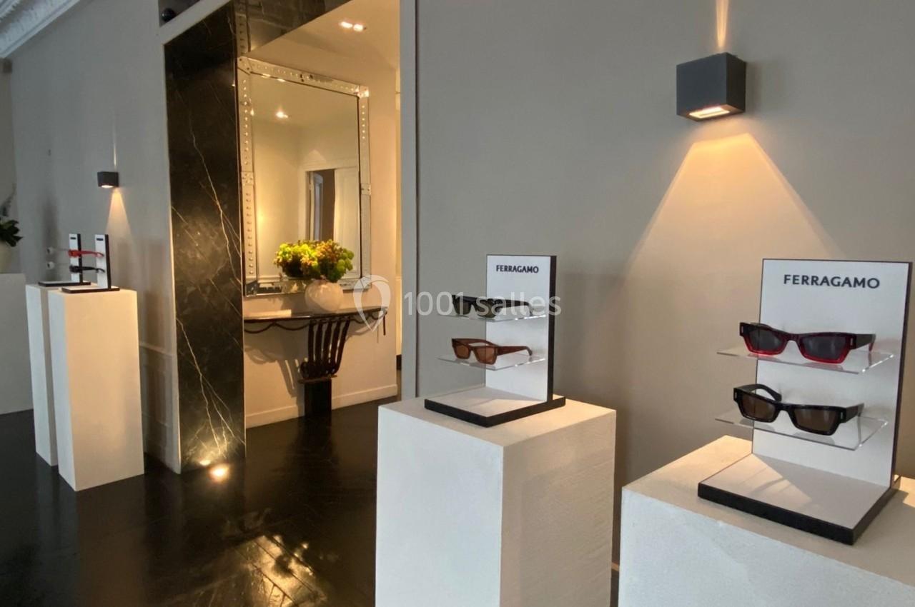 Présentoirs de lunettes de soleil sur des socles blancs dans une pièce élégante avec un grand miroir et un éclairage tamisé.