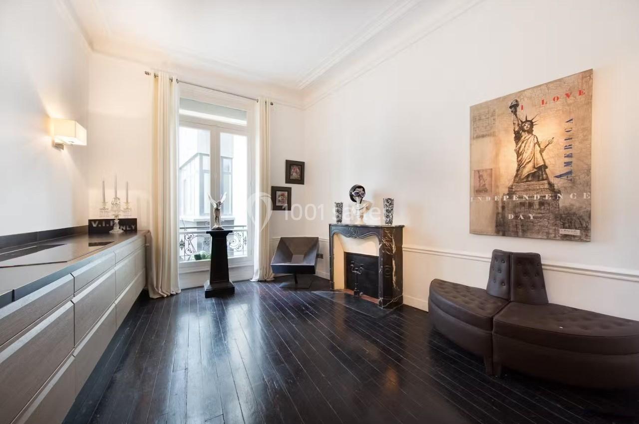 Salon lumineux avec parquet sombre, cheminée décorative, fauteuils modernes et œuvres d'art accrochées aux murs.