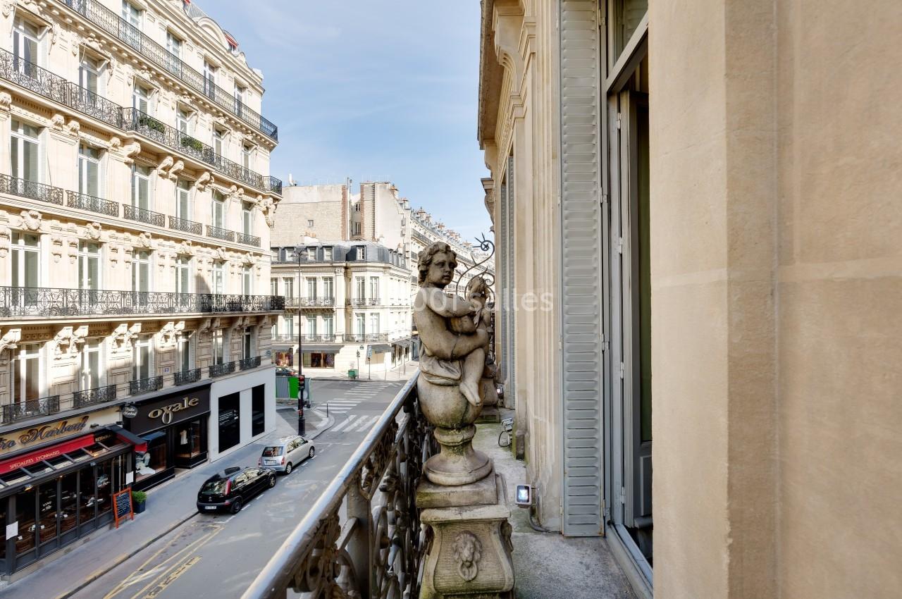 Vue depuis un balcon parisien avec une statue décorative, donnant sur une rue bordée d'immeubles haussmanniens.