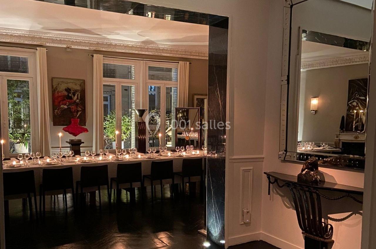 Salle à manger élégante avec une longue table dressée, éclairée par des bougies, entourée de grandes fenêtres et miroirs.