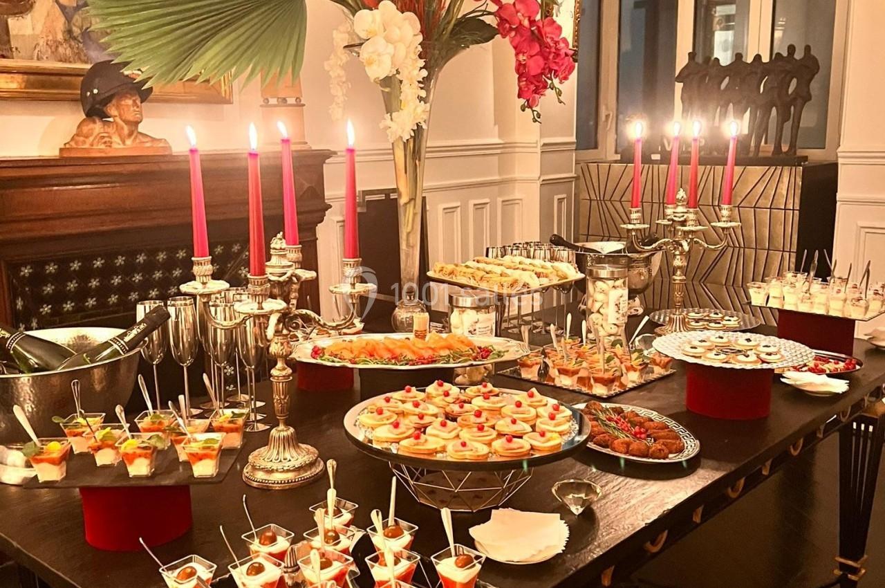 Table garnie de desserts variés, verrines et bougies allumées, décorée de fleurs tropicales dans un intérieur élégant.