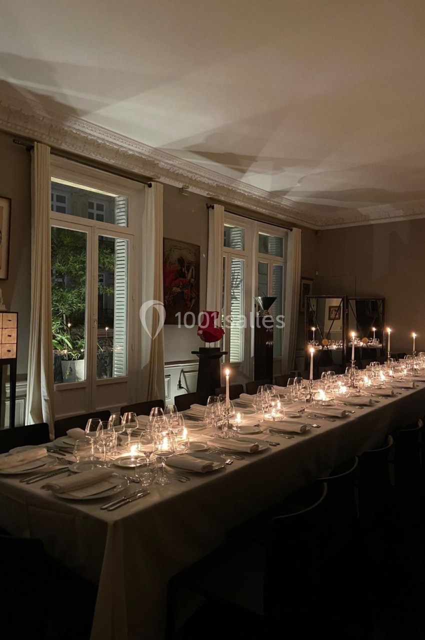 Table élégamment dressée pour un dîner aux chandelles dans une salle à manger tamisée avec vue sur un jardin.