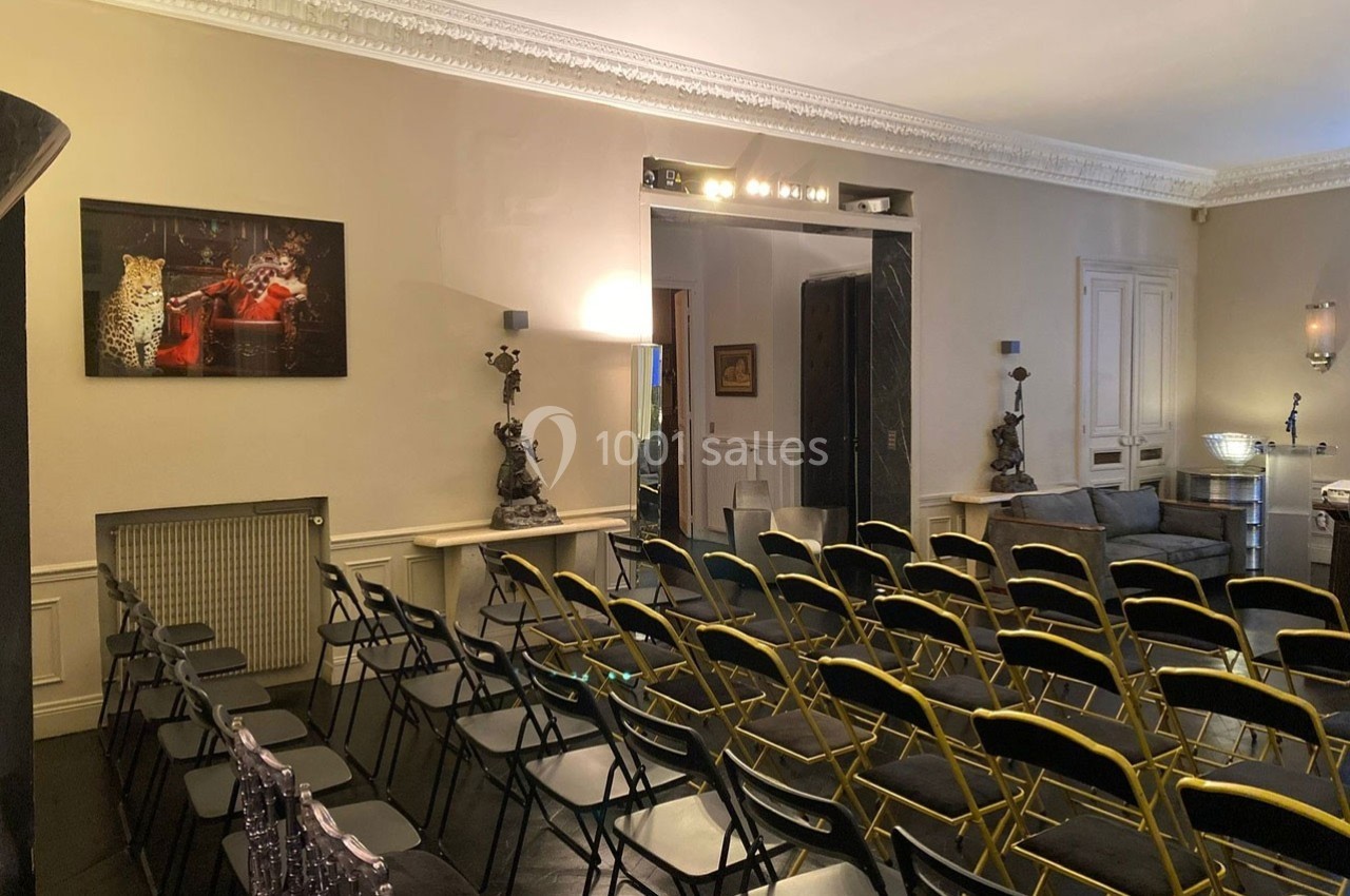 Salle aménagée avec des rangées de chaises pliantes noires et dorées, décorée de tableaux et d'objets d'art.