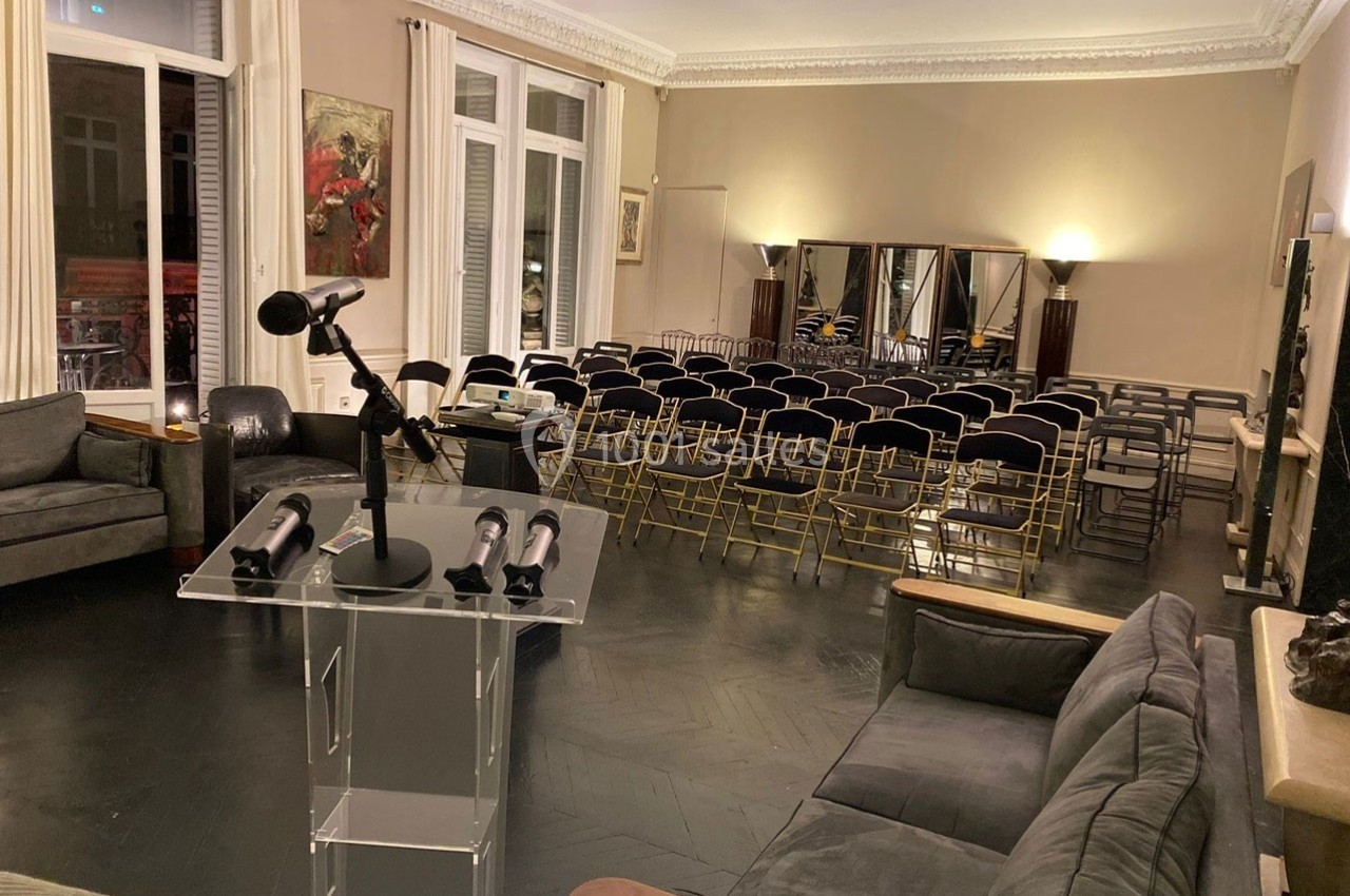 Salle de conférence avec chaises alignées, pupitre transparent équipé d’un micro, dans un intérieur élégant.