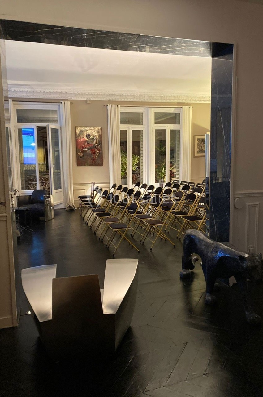 Salle avec des chaises pliantes alignées, éclairée par des baies vitrées, décorée de tableaux et d'une sculpture de panthère.