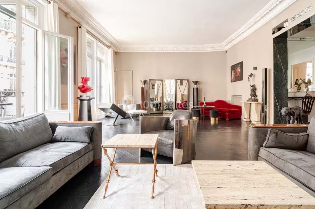 Salon spacieux avec canapés gris, fauteuils modernes, tables basses, et décoration éclectique dans un intérieur lumineux.