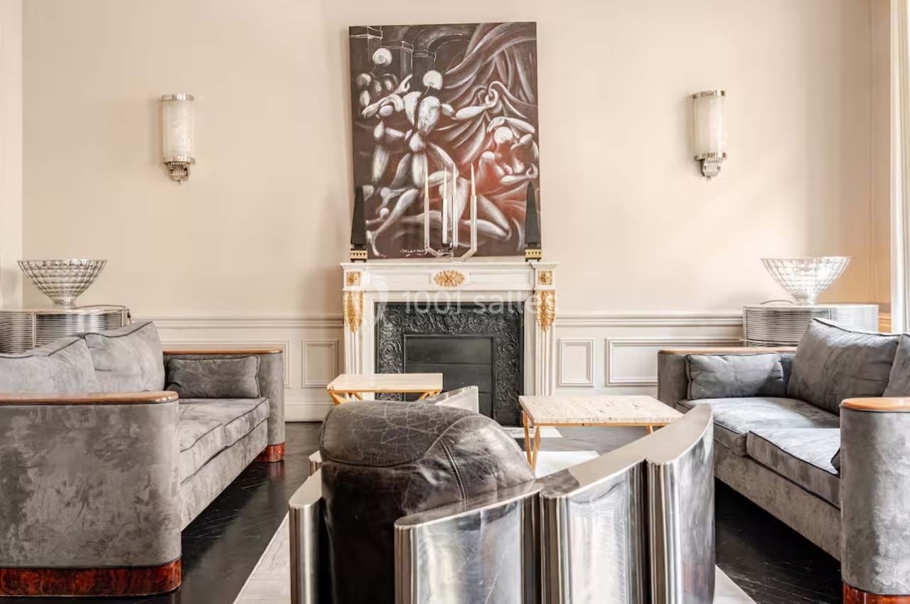 Salon élégant avec canapés gris, cheminée ornée, tableau abstrait au mur et éclairage mural discret.