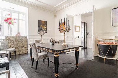 Salle à manger élégante avec table noire ornée, chandeliers, sculpture de panthère et tableau coloré au mur.