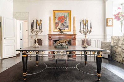 Salle à manger élégante avec table noire ornée, chandeliers, sculpture de panthère et tableau coloré au mur.