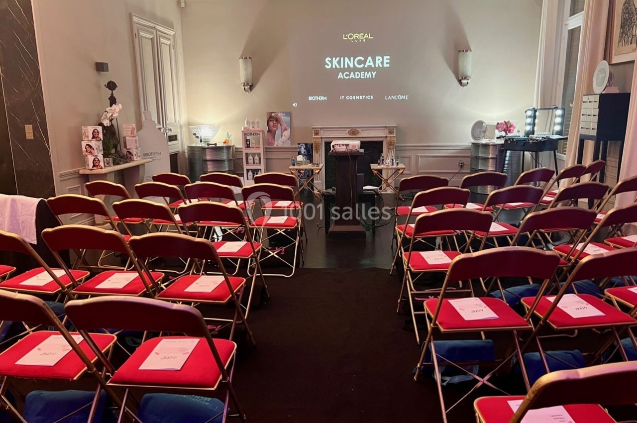 Salle de conférence avec des rangées de chaises rouges, un écran de projection et du matériel de présentation.