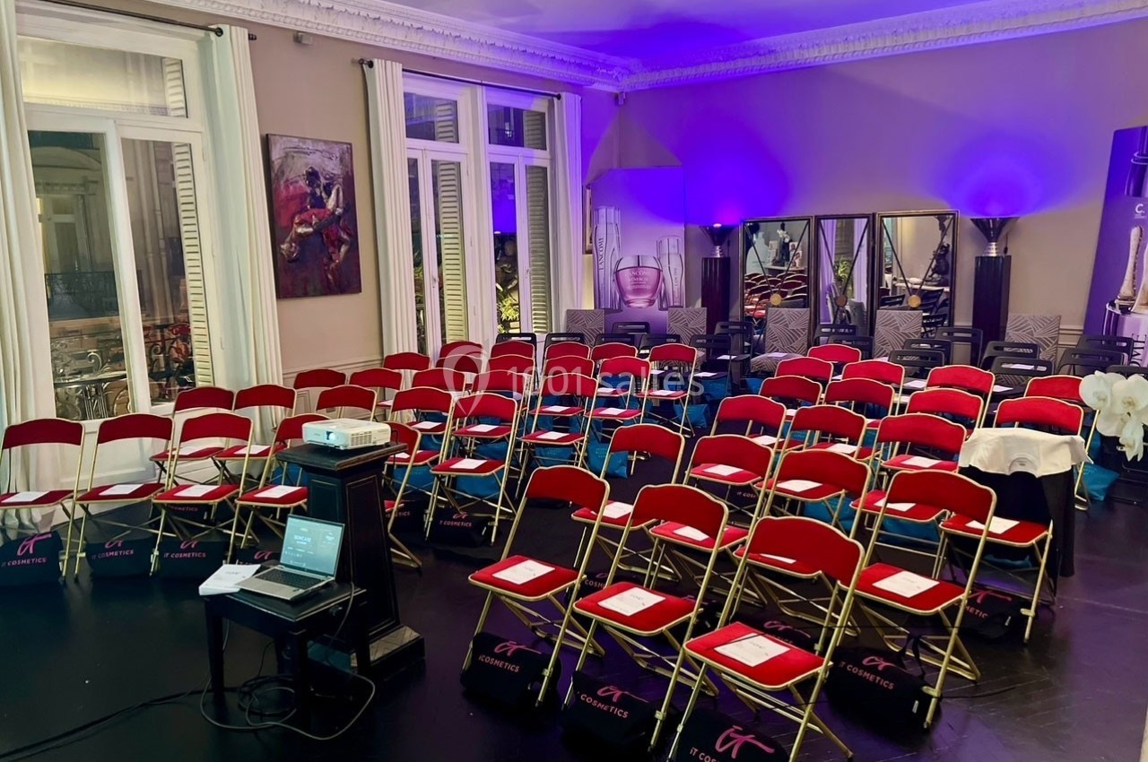 Salle de conférence avec des chaises rouges alignées, un projecteur et des documents disposés pour une présentation.