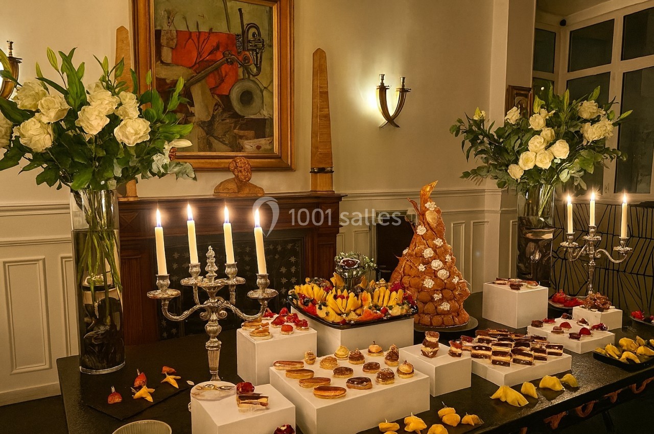 Table décorée avec des chandeliers, fleurs blanches et desserts variés, dont une pièce montée, dans une salle élégante.