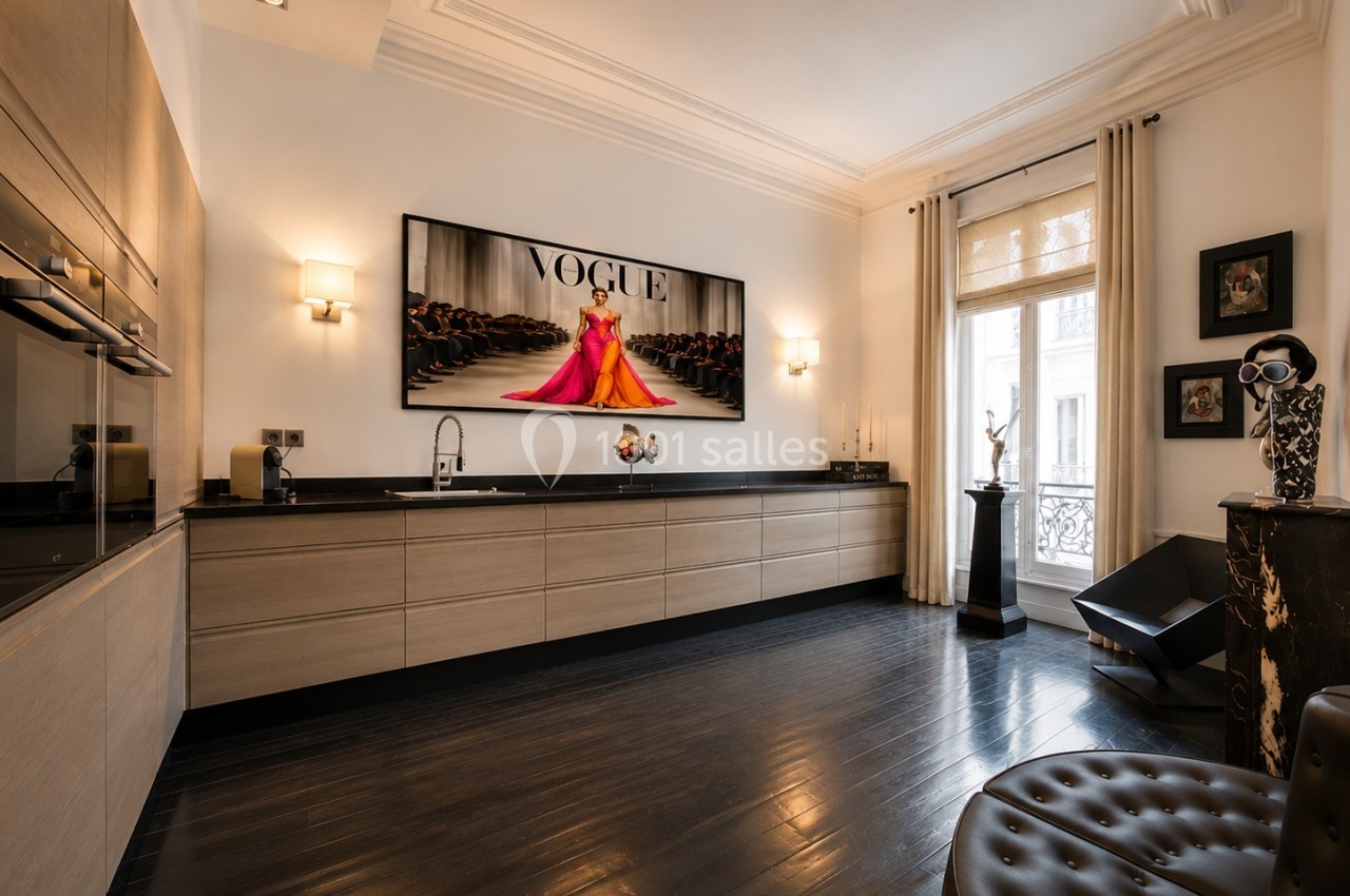 Cuisine moderne avec parquet sombre, meubles en bois clair, tableau mural et grande fenêtre laissant entrer la lumière.