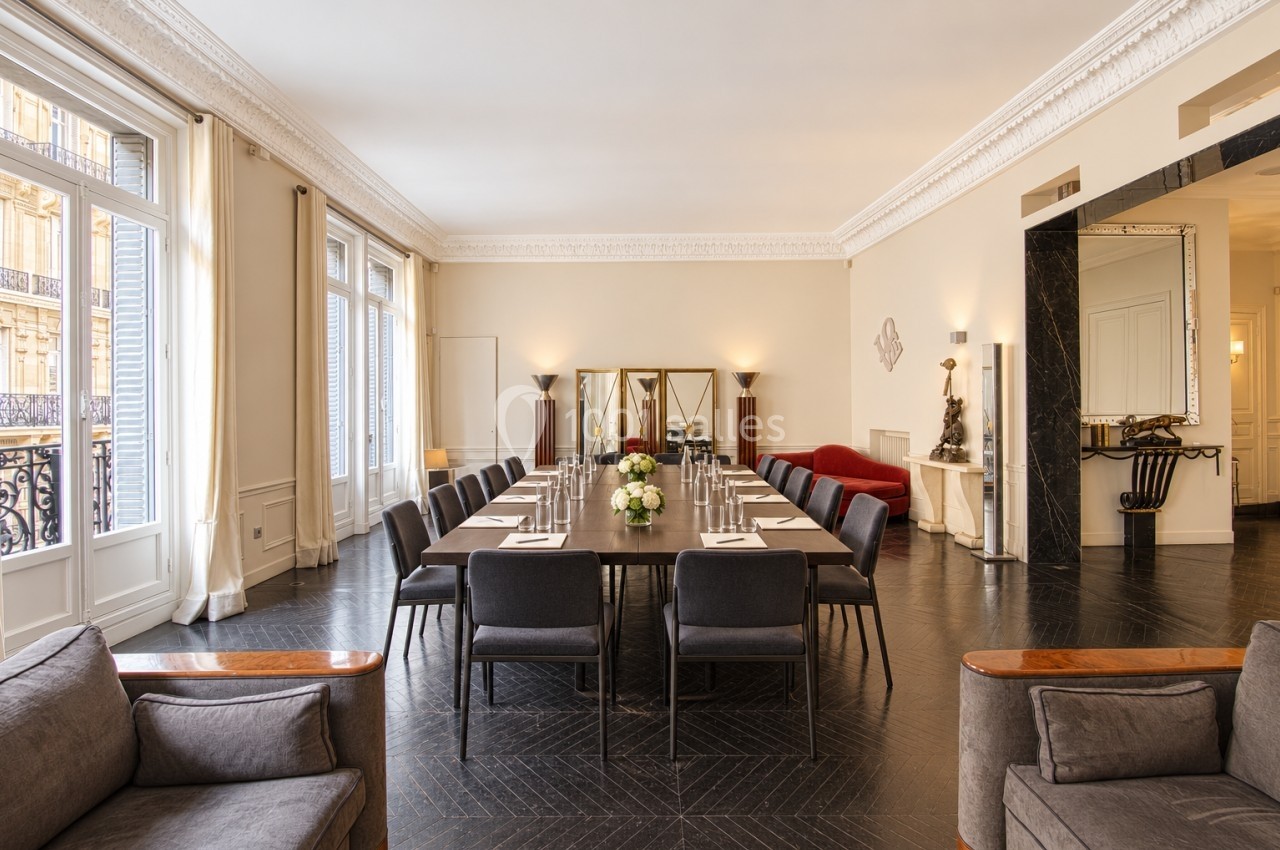 Salle de réunion élégante avec grande table rectangulaire, chaises noires, lumière naturelle et décor raffiné.