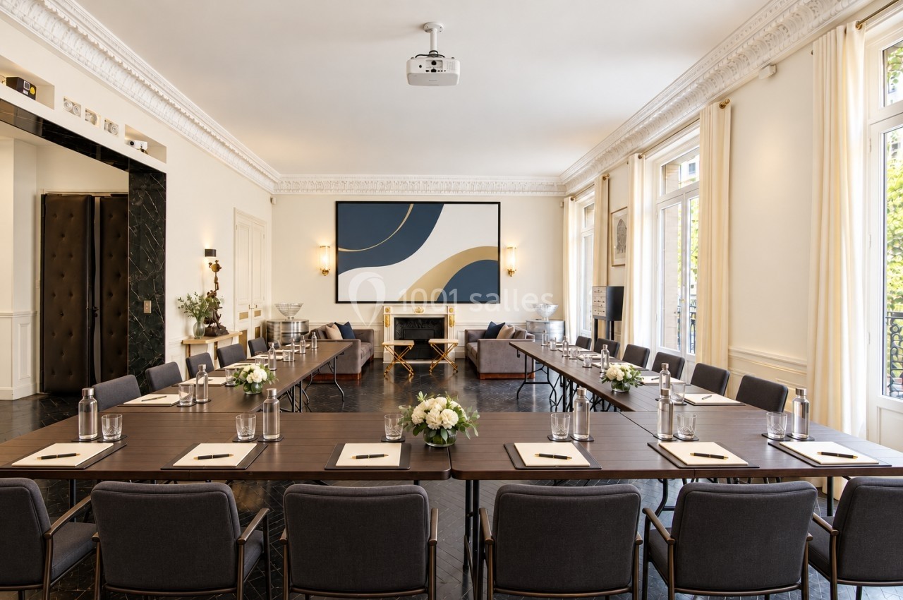 Salle de réunion lumineuse avec tables en U, chaises grises, décor élégant et grandes fenêtres laissant entrer la lumière…