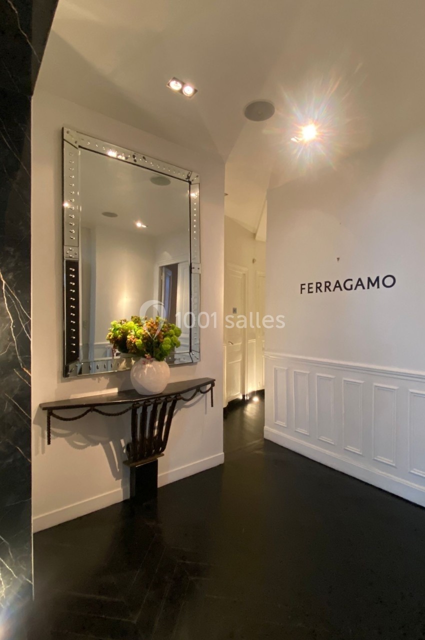 Entrée élégante avec un miroir encadré, une console décorée de fleurs et un mur portant le logo Ferragamo.