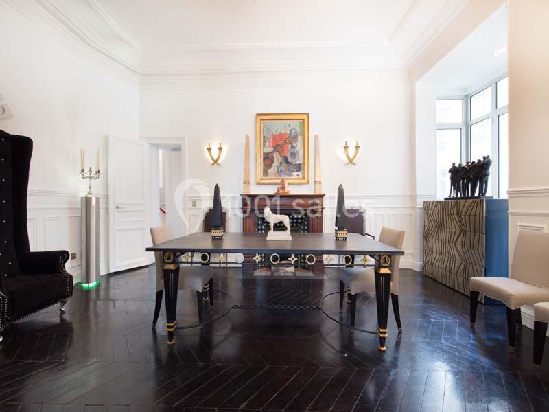 Salle à manger élégante avec table noire ornée, parquet foncé, murs blancs et décoration artistique.