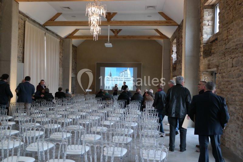Salle de conférence avec des chaises transparentes, un écran de projection allumé et des participants debout.