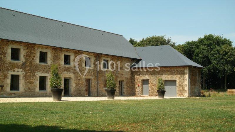 Bâtiment en pierre rénové avec toiture en ardoise, entouré de pelouse et de grands arbres en arrière-plan.