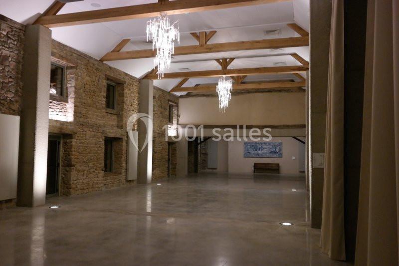 Salle spacieuse avec murs en pierre apparente, poutres en bois au plafond et lustres modernes suspendus.