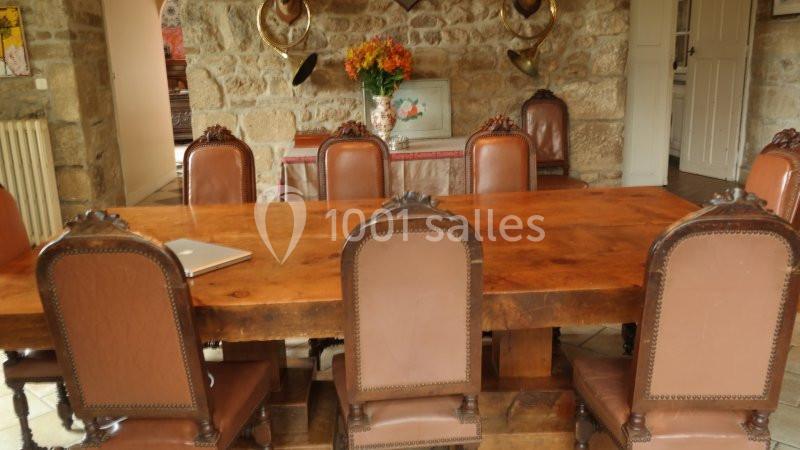 Grande table en bois entourée de chaises en cuir, dans une pièce rustique avec murs en pierre et décoration murale.