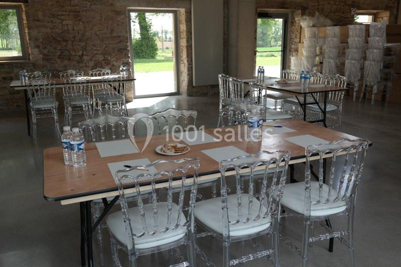 Salle avec des tables en bois, chaises transparentes, bouteilles d'eau, feuilles et stylos, dans un cadre lumineux.