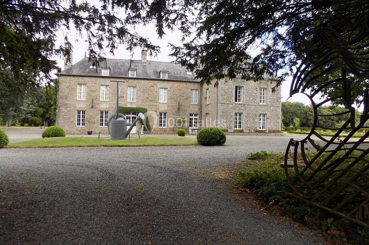 Façade d'un bâtiment en pierre entouré d'arbres, avec une sculpture moderne et une allée gravillonnée au premier plan.