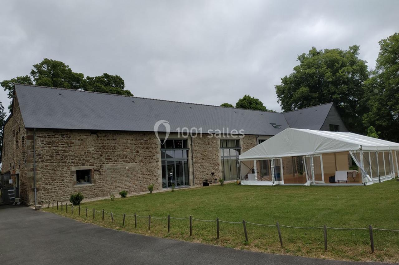 Bâtiment en pierre avec toit en ardoise, adjacent à une tente blanche installée sur une pelouse.