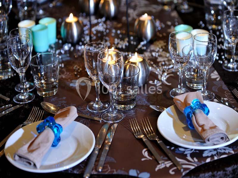 Table élégamment dressée avec des assiettes, verres, couverts, serviettes pliées et bougies allumées en décoration.