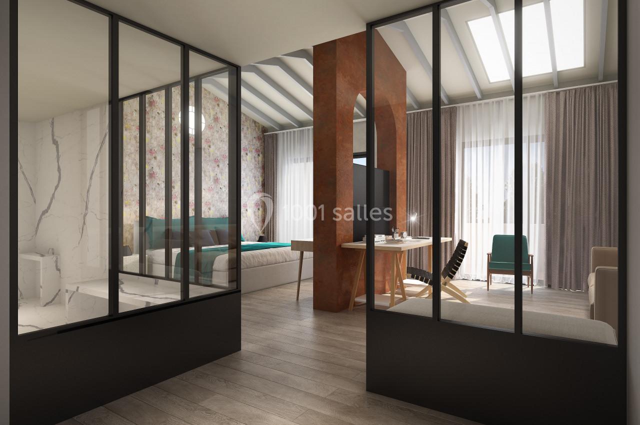 Vue intérieure d'un espace moderne avec une cloison vitrée séparant une chambre et un salon lumineux.