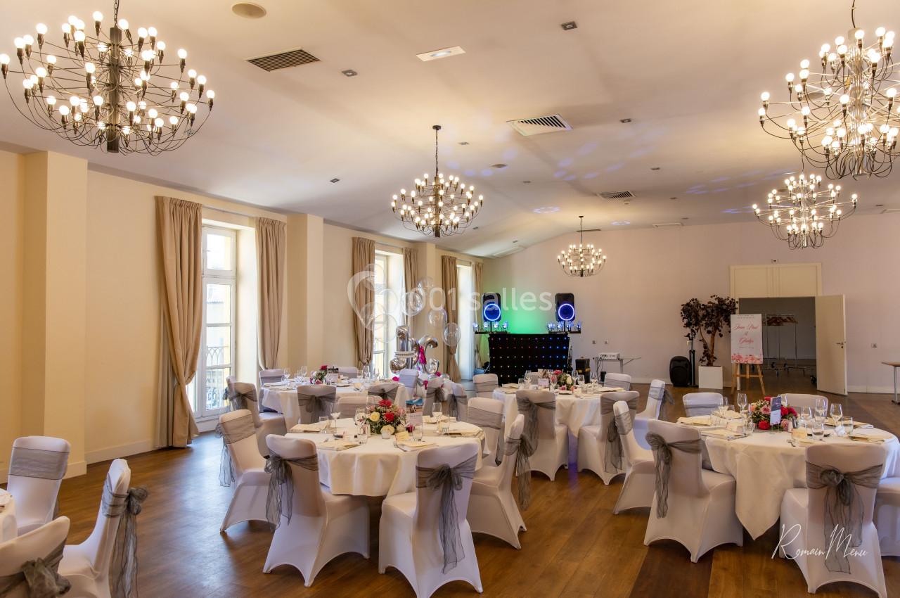 Salle de réception élégante avec tables décorées, chaises couvertes et éclairage tamisé, prête pour un événement.