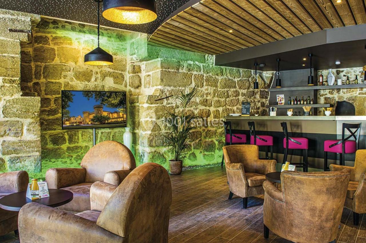 Salon chaleureux avec fauteuils en cuir, tables basses, bar moderne et murs en pierre apparente.