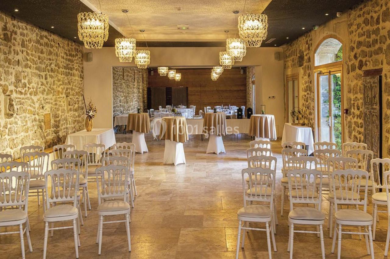 Salle de réception en pierre avec chaises alignées, tables dressées et lustres suspendus.