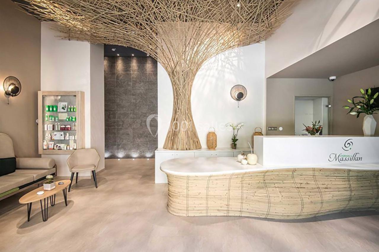Accueil d'un spa avec comptoir en bois, fauteuils, étagère de produits, et décoration évoquant un arbre.