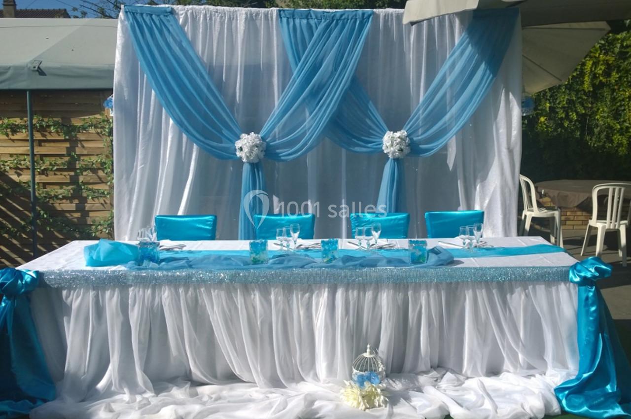 Table décorée pour un mariage avec nappes blanches, drapés bleus, chaises assorties et une cage décorative au sol.