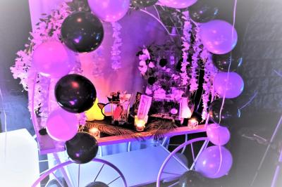 Salle de réception décorée en noir et blanc avec tables dressées, chaises blanches et lanternes suspendues.